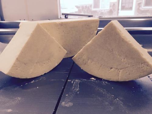 Three large wedges of cheese on a countertop, with a light-colored, smooth surface.
