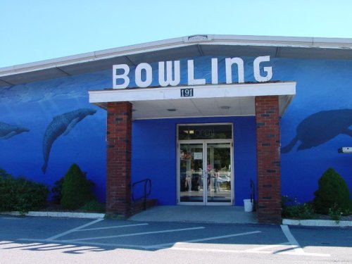 A bowling alley with a blue exterior featuring a mural of dolphins and large "BOWLING" letters above the entrance.