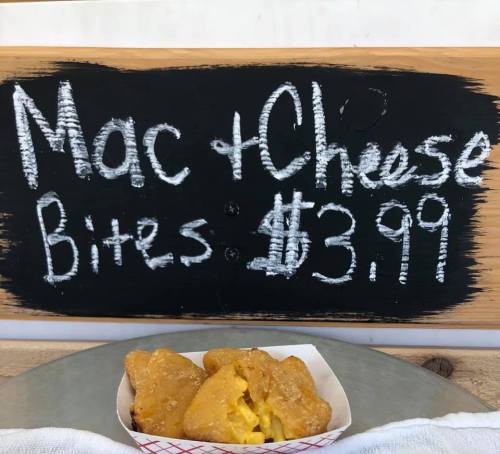 Chalkboard sign displaying "Mac & Cheese Bites" for $3.99, with a serving of golden-brown bites in a paper tray.