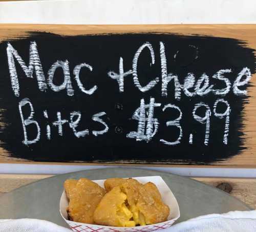 Chalkboard sign displaying "Mac & Cheese Bites" for $3.99, with a serving of golden-brown bites in a paper tray.