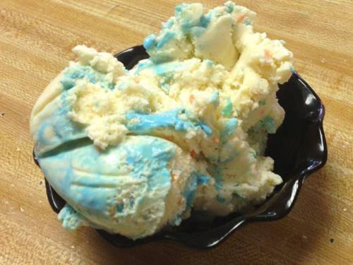 A black bowl filled with colorful ice cream, featuring blue and white swirls with bits of orange.