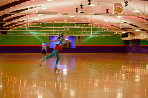 A girl in colorful attire roller skates gracefully in an empty rink with vibrant walls and soft lighting.