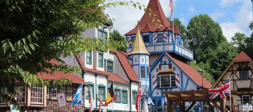 A colorful, European-style village with distinct architecture and flags, set against a blue sky and green trees.