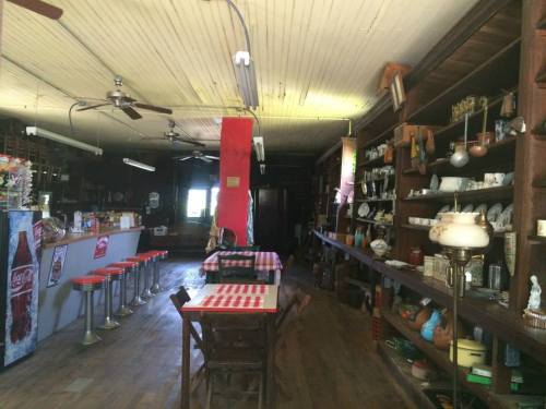 Interior of a vintage diner with red and white checkered tables, a long bar, and shelves filled with antiques.