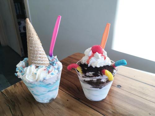 Two colorful ice cream desserts in cups: one with a cone and sprinkles, the other with whipped cream and gummy candies.