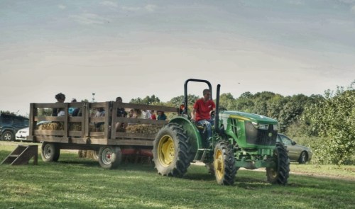 A tractor pulls a hayride with children seated on a wooden trailer in a grassy field.