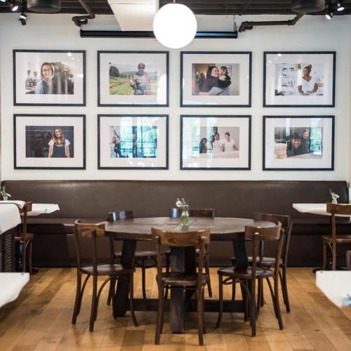 A cozy restaurant interior featuring a round table surrounded by chairs and framed photos on the wall.