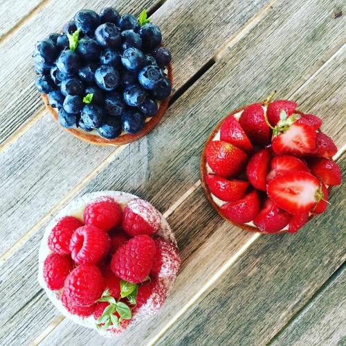 Three fruit tarts topped with blueberries, strawberries, and raspberries on a wooden surface.