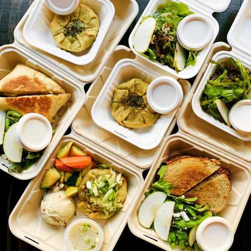 A variety of colorful, neatly arranged food containers with salads, wraps, and dips on a wooden surface.