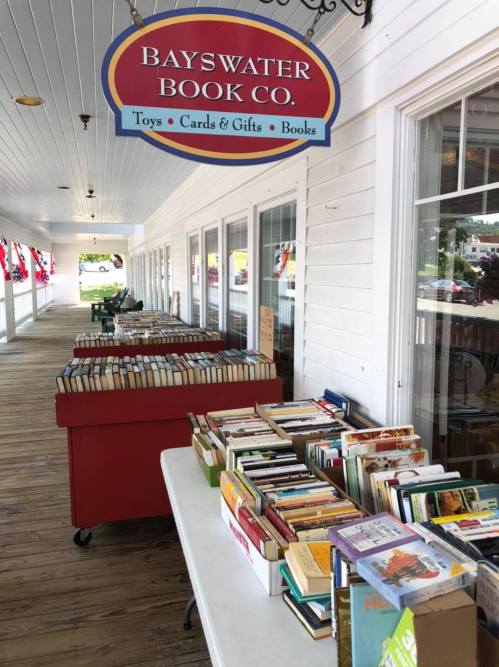 A table filled with books outside the Bayswater Book Co., with a sign above and a porch in the background.