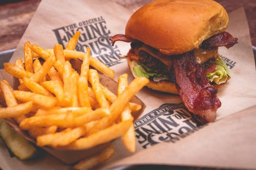 A juicy burger with bacon and lettuce, served with a side of golden French fries on a tray.