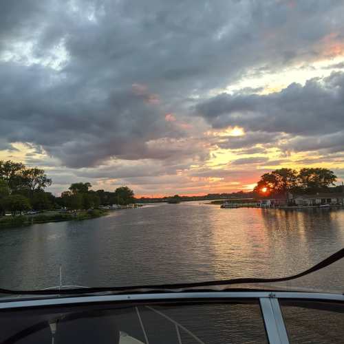 A scenic view of a river at sunset, with clouds reflecting on the water and trees lining the shore.