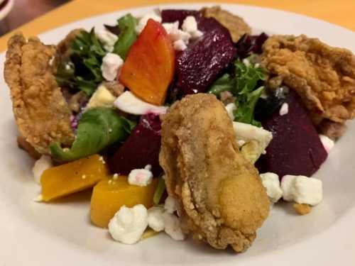 A colorful salad with greens, beets, fried chicken, and crumbled cheese on a white plate.