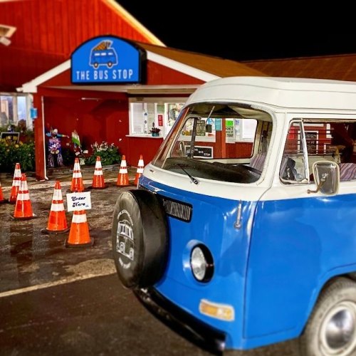 A blue vintage bus parked in front of a red building labeled "The Bus Stop," surrounded by traffic cones at night.