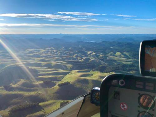 Aerial view of rolling green hills under a clear sky, with sunlight streaming through clouds and a cockpit in the foreground.