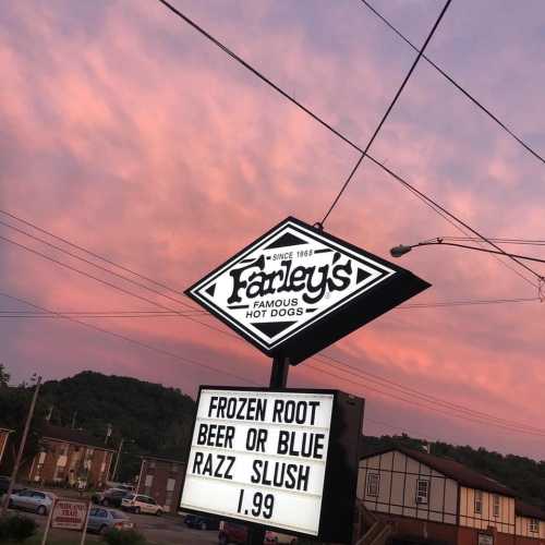 Sign for Farley's Famous Hot Dogs featuring a colorful sunset, advertising frozen root beer slush for $1.99.