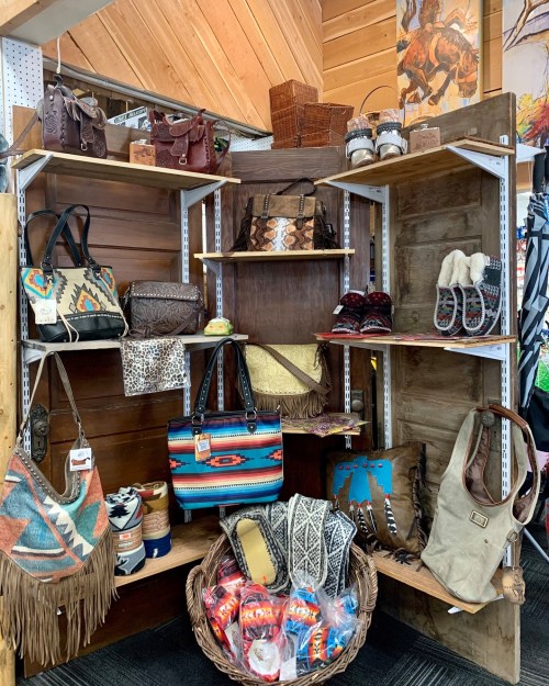 A display of various handbags, purses, and accessories on wooden shelves, featuring colorful patterns and textures.