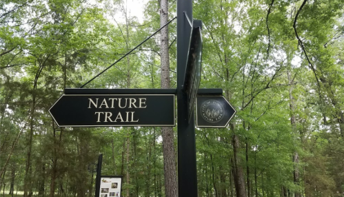 Signpost indicating a nature trail, surrounded by lush green trees in a forested area.