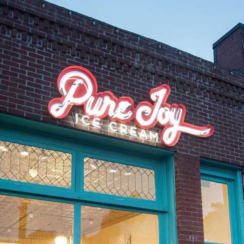 Sign for "Pure Joy Ice Cream" on a brick building, featuring bright neon lettering and a turquoise trim.