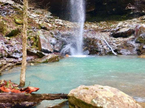 A serene waterfall cascades into a turquoise pool, surrounded by rocky terrain and lush greenery.