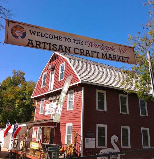 Sign for War Eagle Mill Artisan Craft Market, featuring a red building and trees in the background.