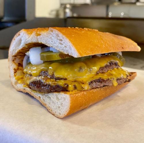 A close-up of a cheeseburger in a toasted bun, topped with pickles and onions, resting on a piece of parchment paper.