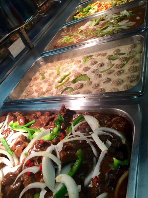 A buffet display featuring various dishes, including meat with vegetables and a creamy sauce, in metal trays.