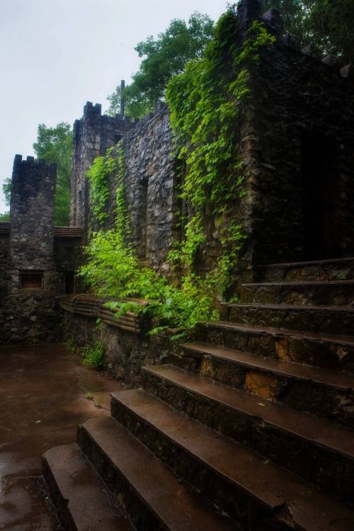 Overgrown stone ruins with moss-covered steps, surrounded by lush greenery and a cloudy sky.