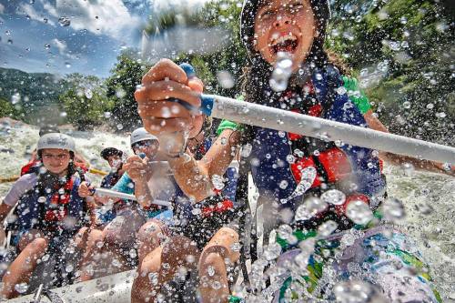 A group of people enjoying white-water rafting, splashed with water and smiling amidst the excitement.