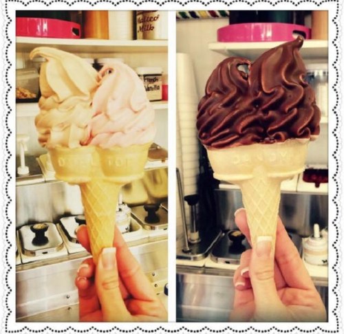Two ice cream cones held by a hand: one with pink soft serve and the other with chocolate soft serve.