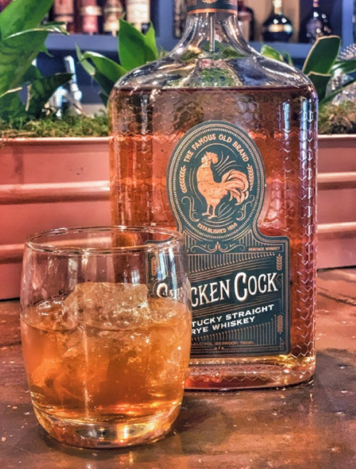 A bottle of Chicken Cock Kentucky Straight Rye Whiskey next to a glass filled with whiskey and ice.
