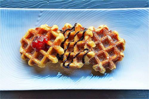 A plate with two waffles drizzled with chocolate and topped with a cherry.