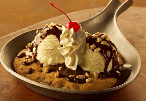 A warm chocolate chip cookie topped with two scoops of ice cream, chocolate sauce, whipped cream, nuts, and a cherry.