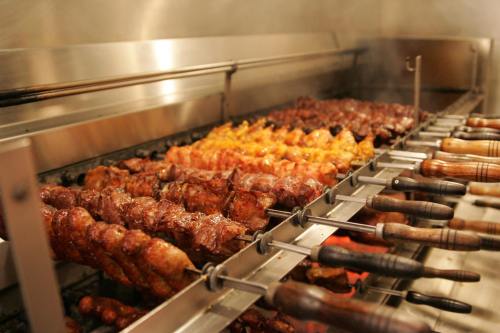 Skewers of grilled meat cooking on a rotisserie, with smoke rising in a restaurant kitchen.