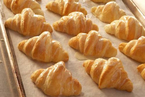 Freshly baked croissants arranged on a baking tray, glistening with a light glaze.