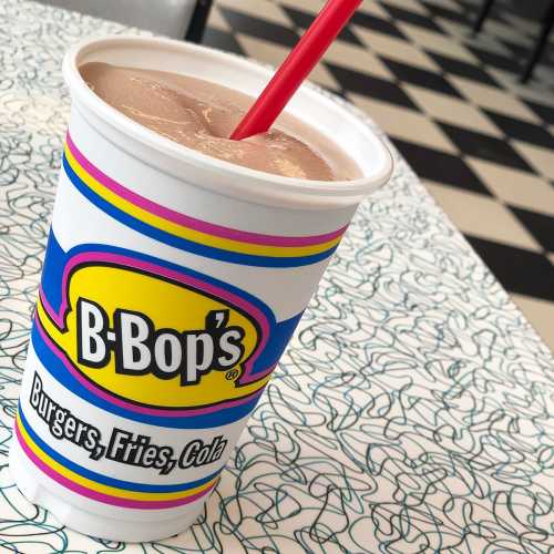 A colorful cup from B-Bop's with a straw, sitting on a checkered table.