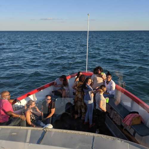 A group of people socializing on a boat, with a clear blue sky and water in the background.