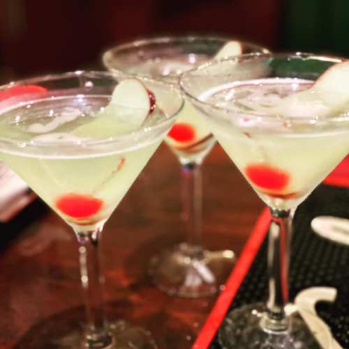 Three green cocktails with cherries, served in martini glasses on a bar counter.