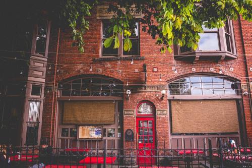 A brick building with a red door and closed windows, surrounded by greenery and outdoor seating.