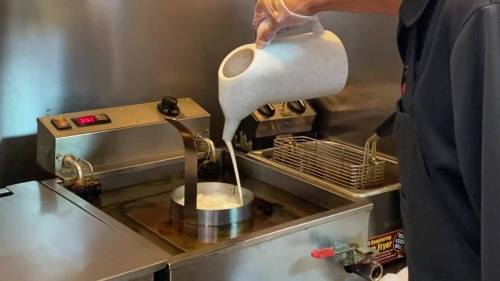 A person pours milk into a frying machine, preparing to cook something in a commercial kitchen.