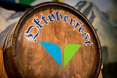 A wooden barrel with the word "Oktoberfest" and a green logo, set against a scenic backdrop.