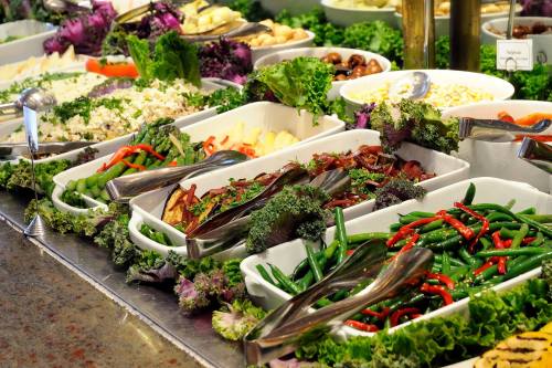 A colorful buffet featuring various salads and vegetables in white dishes, garnished with fresh greens.