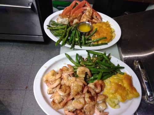 Two plates of seafood: one with shrimp and green beans, the other with crab, green beans, and cheesy casserole.