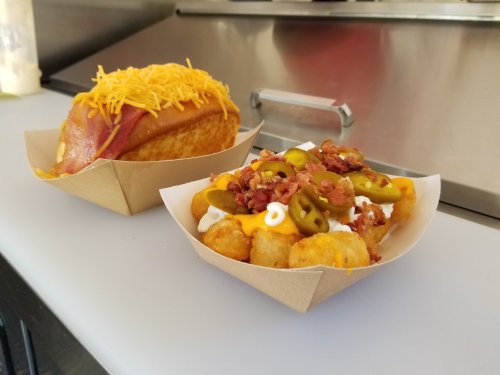 A plate with a cheesy hot dog and a serving of loaded tater tots topped with bacon and jalapeños.
