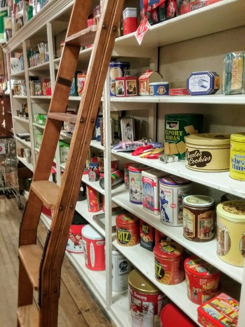 A wooden ladder beside shelves filled with colorful vintage tins and containers in a nostalgic store setting.