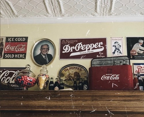 Vintage display featuring Dr. Pepper and Coca-Cola memorabilia, including signs, bottles, and a portrait on the wall.