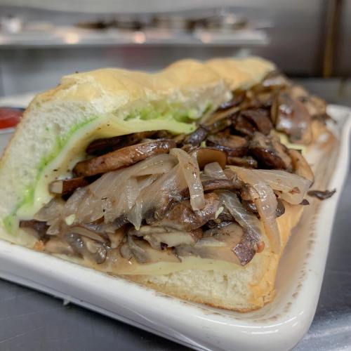 A close-up of a sandwich filled with mushrooms, cheese, and lettuce on a toasted hoagie roll.