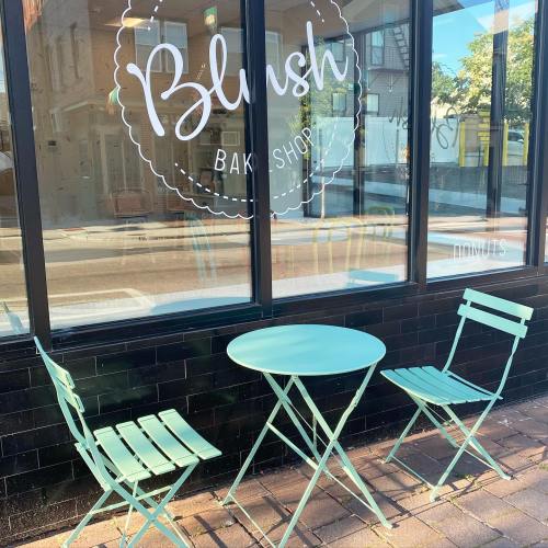 A pastel blue table and chairs outside a bakery with a sign that reads "Blush Bakery Shop."