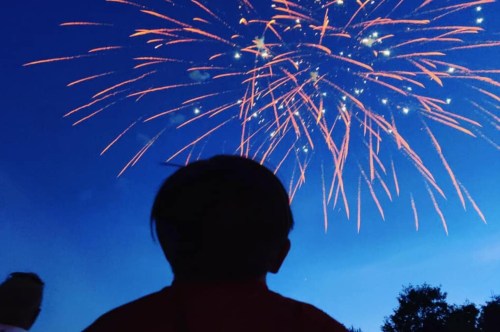 A silhouette of a child watching colorful fireworks against a dark blue sky.