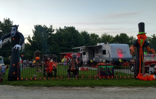 A festive Halloween display with inflatable decorations, a decorated fence, and a camper in the background.
